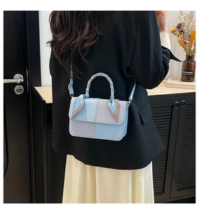 Detail of light blue paneled handbag featuring textured fabric and silk scarf handle