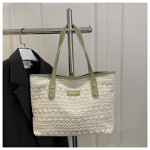 Detail of hollow-out woven tote bag featuring green leather handles and brand logo