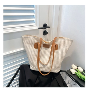 Détail du sac cabas tissé beige avec anses en cuir marron posé sur une chaise