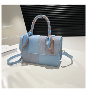 Detail of light blue handbag featuring mixed textures and decorative silk scarf handle