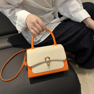 Detail of orange leather crossbody bag with white woven flap and metal teardrop lock