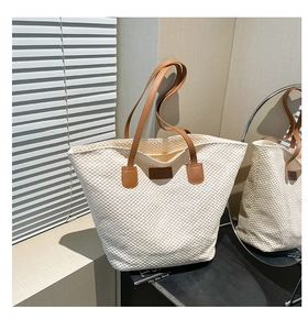 Détail du sac seau en paille tissée avec lanières en cuir marron sous lumière naturelle