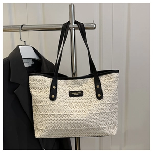 Detail of hollow woven tote bag featuring black leather handles and golden rivets