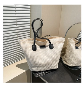Détail d'un sac cabas tissé crème avec anses en cuir noir et lumière naturelle