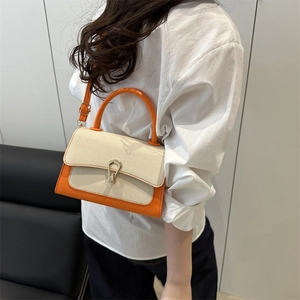 Detail of crossbody bag featuring orange leather, woven lid texture and gold metal buckle