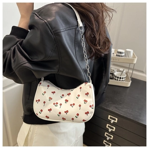 Détail d'un sac à bandoulière blanc avec imprimés cerises rouges et chaîne en métal argenté