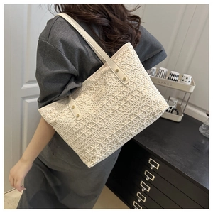 Detail of hollow woven straw tote bag with beige leather straps and gold rivet accents