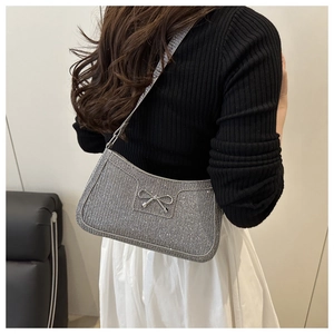 Sac porté épaule à paillettes argentées avec nœud, porté par un mannequin en tenue décontractée