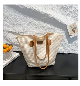 Détail du sac cabas en paille avec écusson en cuir marron et bandoulière en similicuir