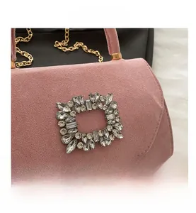 Close-up of pink suede handbag featuring a large square crystal buckle and gold chain
