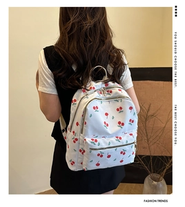 Detailed view of white nylon backpack with cherry pattern and secure zipper pockets