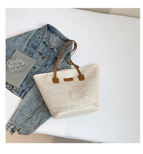 Détail du sac seau tissé crème avec poignées brunes et écusson cuir sur tissu blanc