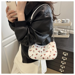 Détail du sac bandoulière blanc à motif cerise avec chaîne argentée porté par un mannequin
