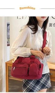 Detail view of burgundy nylon crossbody bag featuring dual front zipper pockets and wide strap