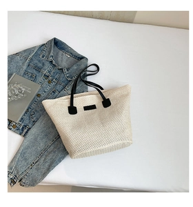 Détail d'un sac seau en paille tressée avec anses noires sur un fond d'été
