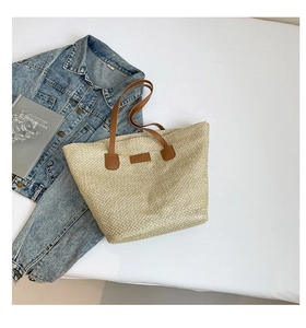 Détail du sac seau en paille tressée avec poignées en cuir sur une veste en jean