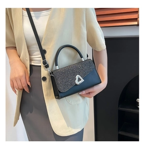 Détail d'un sac à main noir brillant avec boucle coeur argentée et poignée ronde