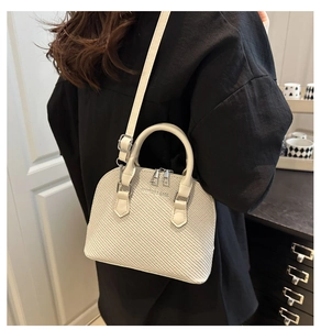 Detail showing shell-shaped cream handbag with textured woven pattern and silver hardware
