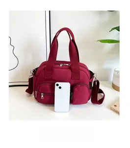 Detail view of large red nylon shoulder bag with multiple zippers and size comparison to phone