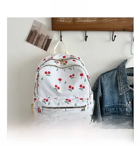 Detailed view of white cherry print nylon backpack hanging on a rustic wooden hook