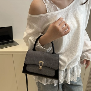 Detail of a two-tone leather crossbody bag featuring a golden trapezoid lock and top handle