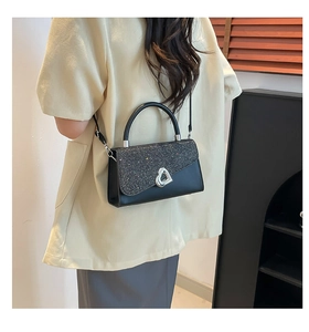 Close-up of black handbag with silver sequin flap and heart-shaped metal lock on model