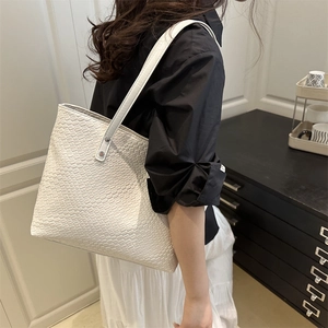 Detailed view of the white woven texture and silver rivet hardware on the tote bag