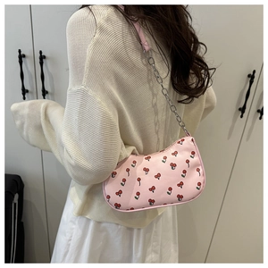 Sac bandoulière rose imprimé cerises avec chaîne métallique porté par un mannequin