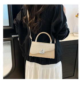 Détail d'un sac bandoulière beige avec rabat pailleté et boucle cœur porté par un mannequin