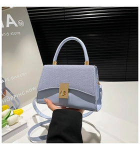 Detail of light blue crossbody bag with textured patchwork and gold metal twist lock closure
