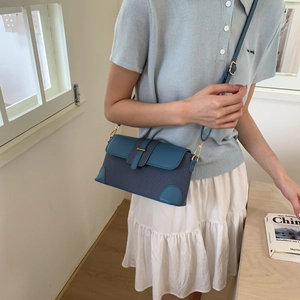 Close-up of blue patchwork small square bag with woven texture and gold metal buckle