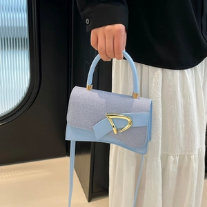 Close-up of light blue crossbody bag with gold D-buckle and sequin patchwork texture