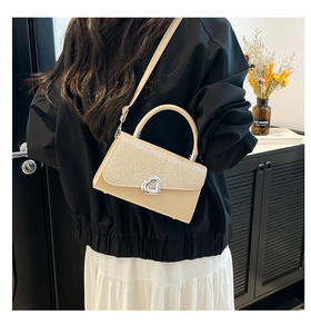 Detail of glitter fabric flap and silver heart-shaped metal lock on cream crossbody bag