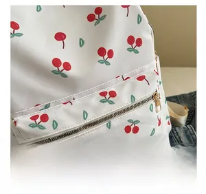 Detail of red cherry print on white nylon backpack with gold zipper and smooth texture