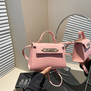Pink woven mini crossbody bag with gold hardware and top handle shown in lifestyle setting