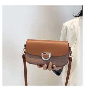 Détail d'un sac porté épaule marron avec boucle en métal argenté sur un manteau blanc