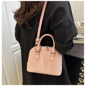 Pink shell handbag with woven texture and crossbody strap worn by a model