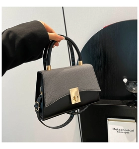Detail of tweed flap texture and golden twist lock on a black contrast crossbody bag