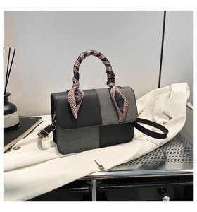 Detail of stylish color-block handbag with silk scarf handle on elegant silk fabric