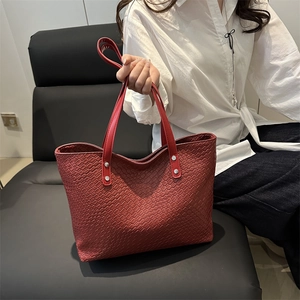 Detail of red tote bag with square embossed texture and silver rivet hardware on handles