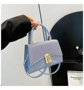Detail of light blue crossbody bag featuring contrast texture and gold twist lock closure