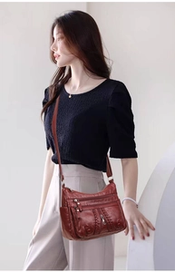 Detail of reddish brown leather crossbody bag with braided texture and multi-zipper pockets