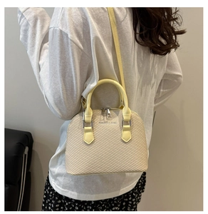 Detail of a beige woven shell bag with yellow leather straps and silver metal logo