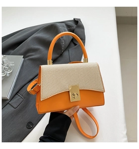 Detail of contrast color square bag with orange leather and woven flap with gold clasp