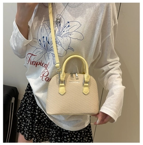 Beige woven shell handbag on model featuring yellow handles and crossbody strap