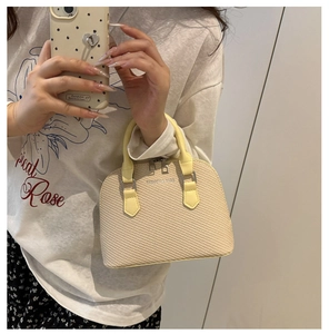 Detail of light yellow woven shell bag featuring a top zipper and sturdy leather handles