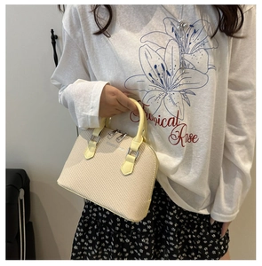 Detail shot of beige textured shell bag with dual handles and silver zipper hardware