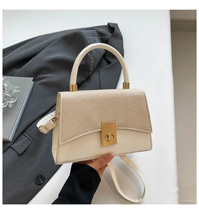 Detail of beige structured handbag with woven flap, gold lock and round top handle