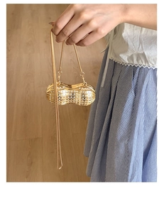 Detailed view of mini peanut-shaped gold evening bag with pearls and long chain strap
