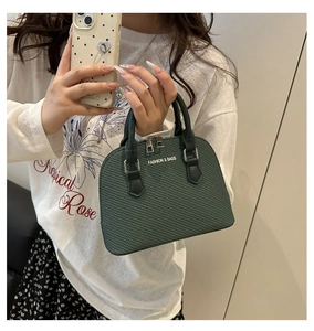 Close-up of a dark green shell bag with woven texture and top handles carried by a model